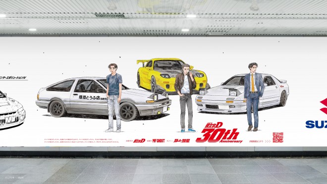 Image of the 22-meter Initial D anniversary ad featuring Shuichi Shigeno’s new Project D illustration, seven iconic cars from the manga, and logos of seven Japanese carmakers, displayed at Shibuya Station in Tokyo.